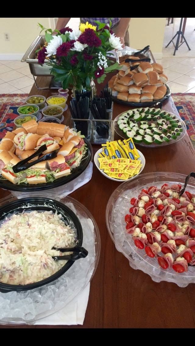 Catering platters of subs and salads arranged around a floral centerpiece