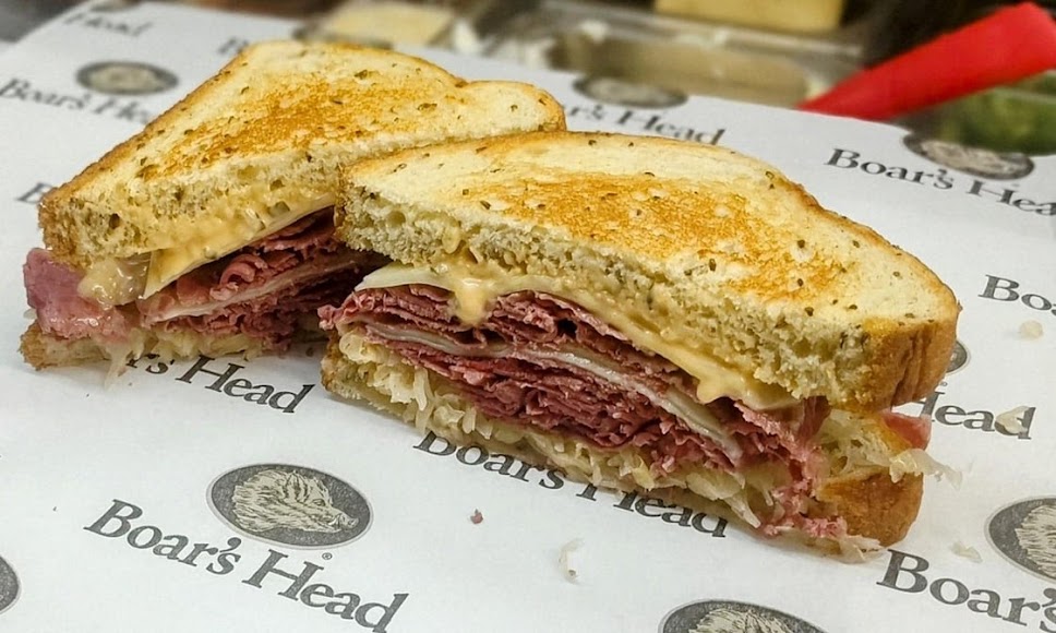 A toasted Reuben with corned beef, cheese and sauerkraut on Boar’s Head paper